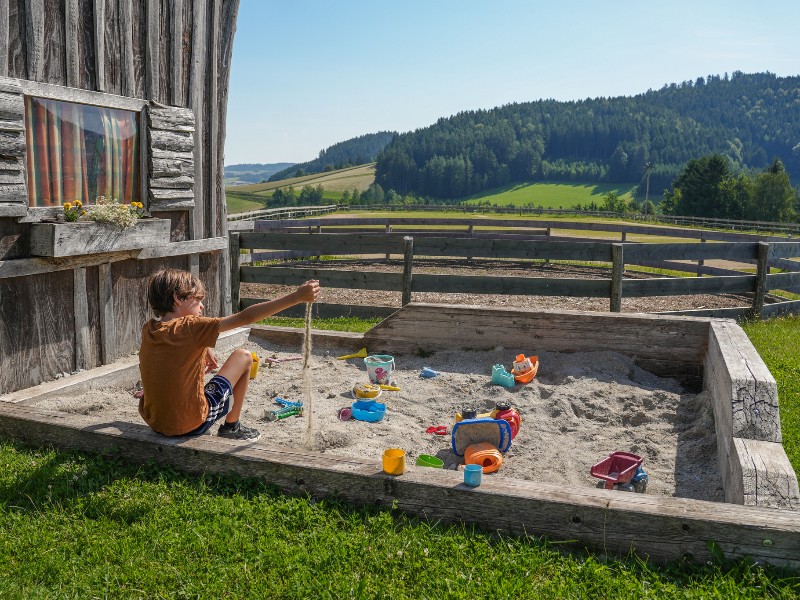 De zoon van Kim kijkt uit over de glooiende heuvels van het Mühlviertel vanaf de zandbak op de Moser Alm